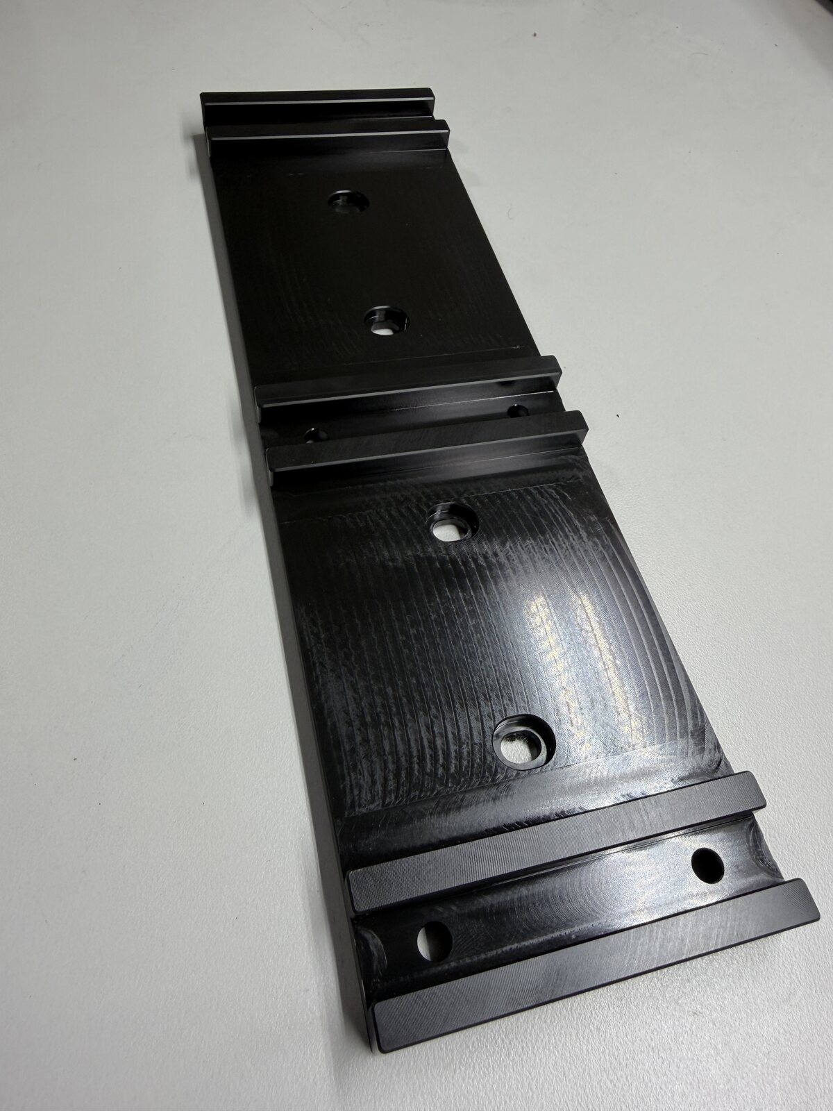 Black anodized aluminum rail with raised mounting features and bores