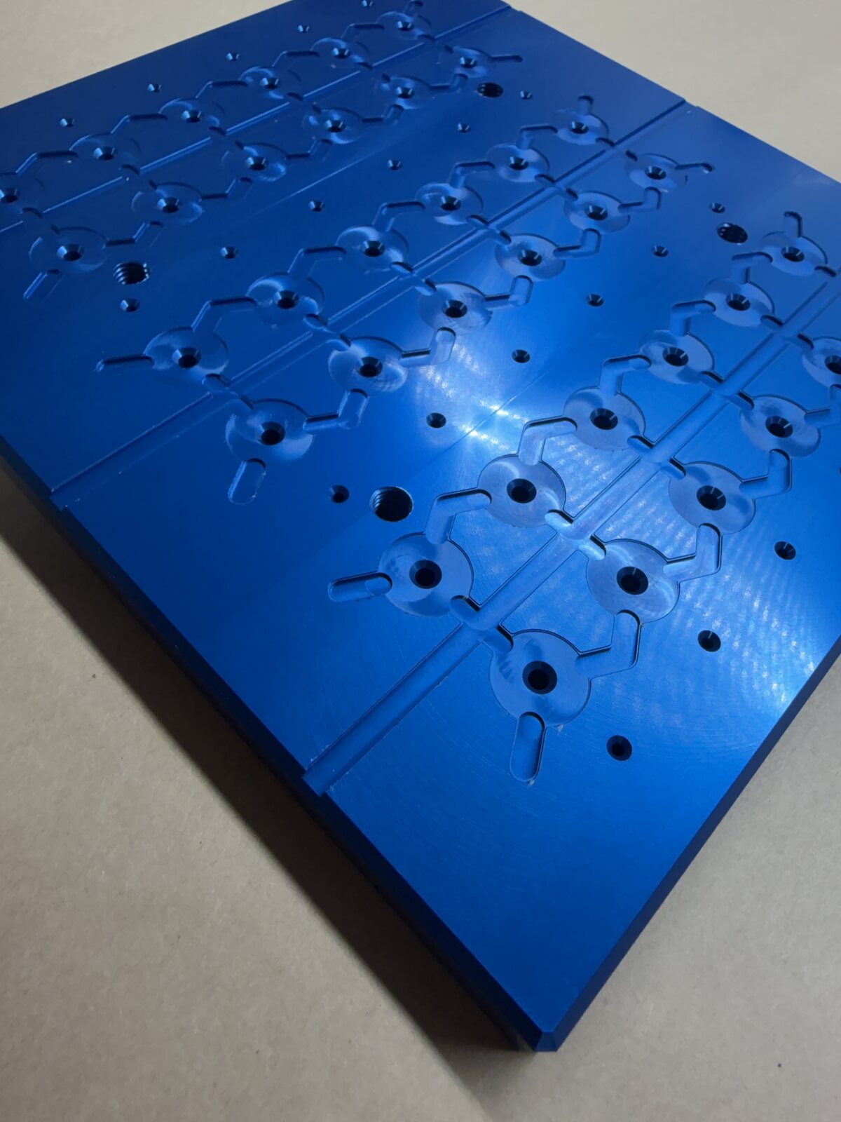 Blue anodized aluminum plate with repeated precision pockets and bores